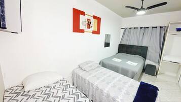 Una habitación con dos camas, ventilador de techo, una obra de arte en la pared y una ventana con cortinas.