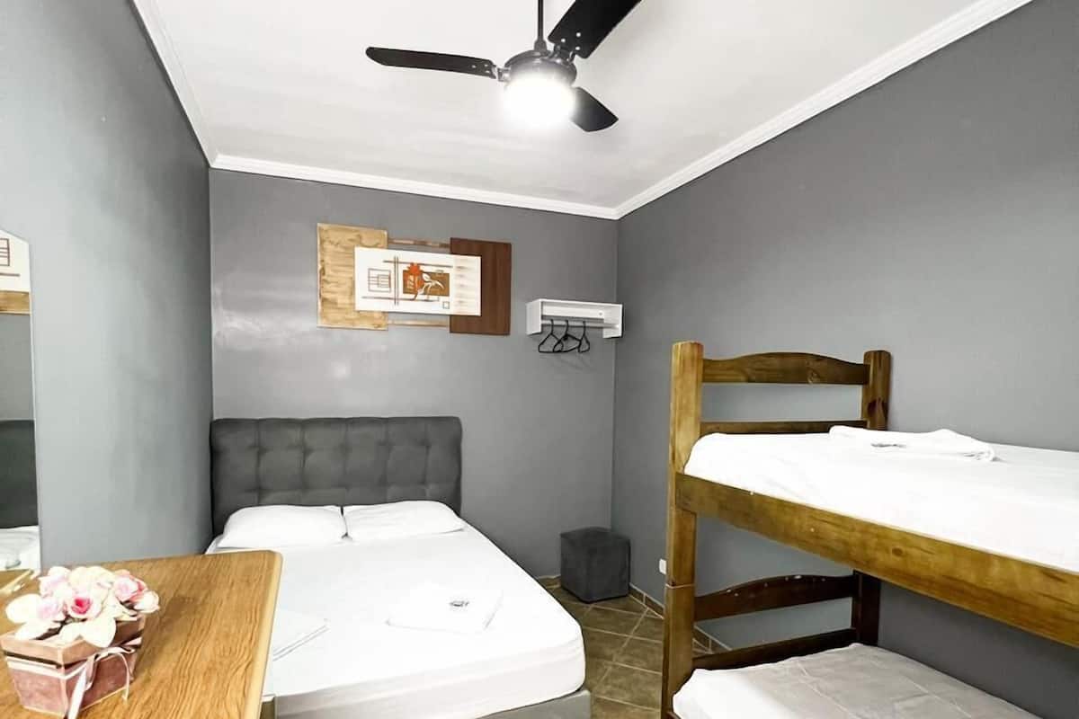 A compact room with a bed, a desk, a bunk bed, a ceiling fan, and a wall-mounted air conditioning unit.