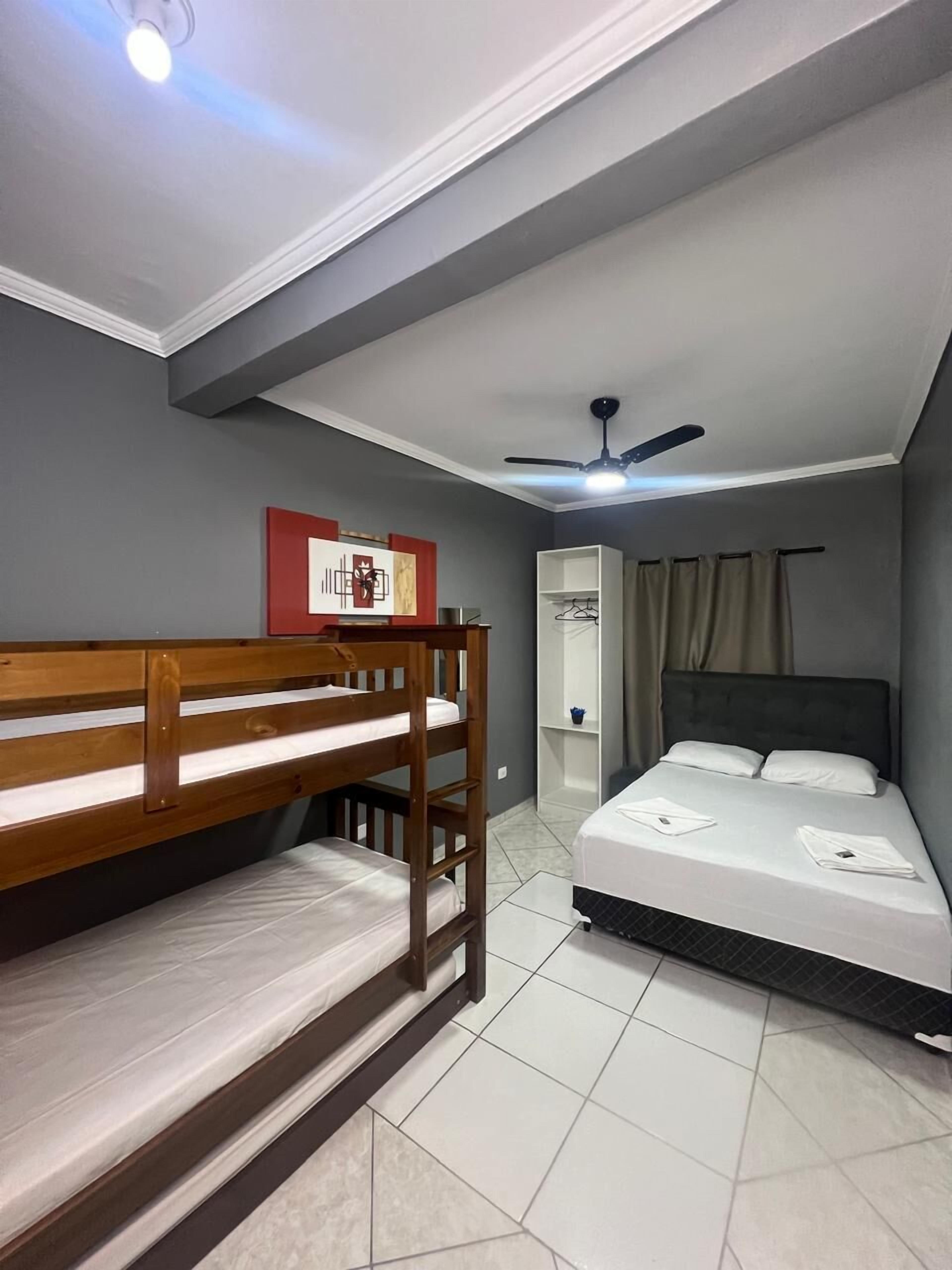 A room with a bunk bed, a single bed, a ceiling fan, and a wall-mounted shelf.