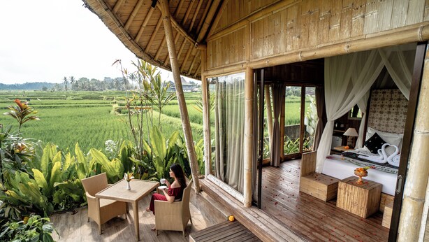 A room with a bed, a small table, and a chair. There is a large window and a view of a green field. - Padi Bali Retreat (Payangan)
