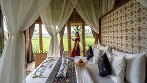 A bedroom with a bed, curtains, a view of a field, and a person standing by the window. - Padi Bali Retreat (Payangan)