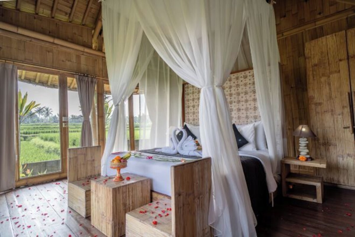 A four-poster canopy bed with a view of a lush landscape, wooden flooring, and a small bedside table with a lamp.