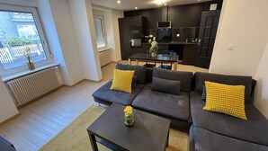 Un saló modern amb un conjunt de sofàs, una taula de centre i una cuina al fons.
