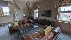A living room with a brown leather sofa, a glass coffee table, and a television mounted on the wall. - Penthouse-highstreet-sleeps2-87ws (Merthyr Tydfil)