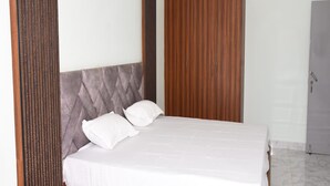 A modern bedroom with a wooden bed frame, a grey upholstered headboard, and a wooden wardrobe. - Maurya Residency (Gingee)