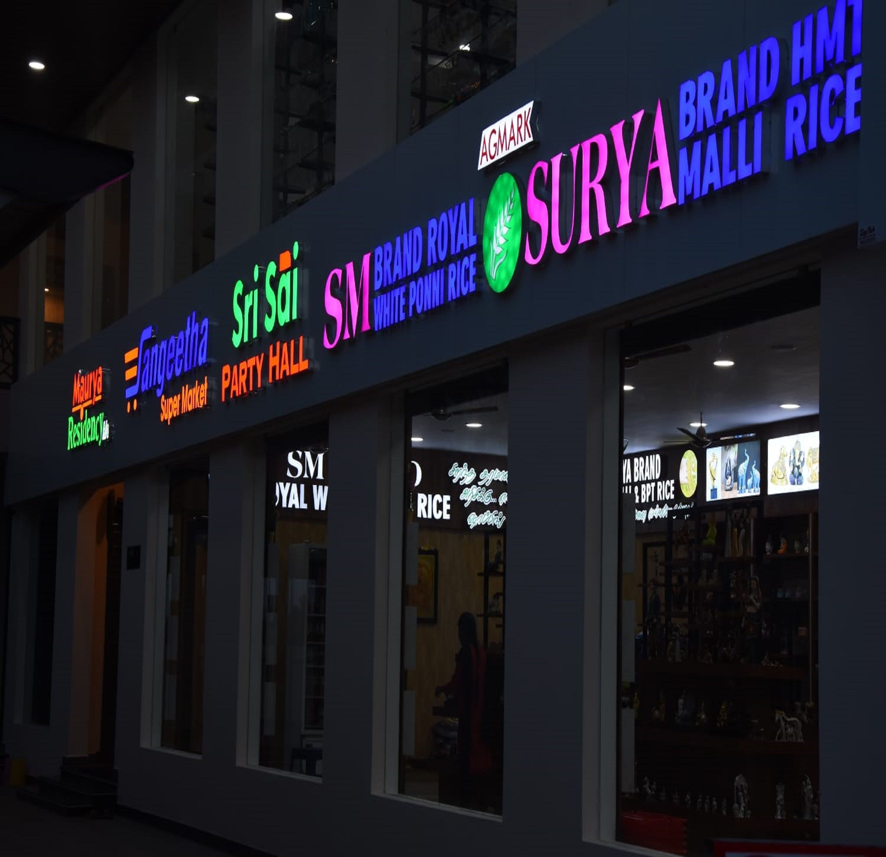 Un immeuble abritant plusieurs commerces, notamment « Sri Sai Super Market », « Sangeetha Super Market », « Party Hall », « SM Brand Royal White Ponna Rice », « Surya Brand HMT Malli Rice » et « Ya Brand ».