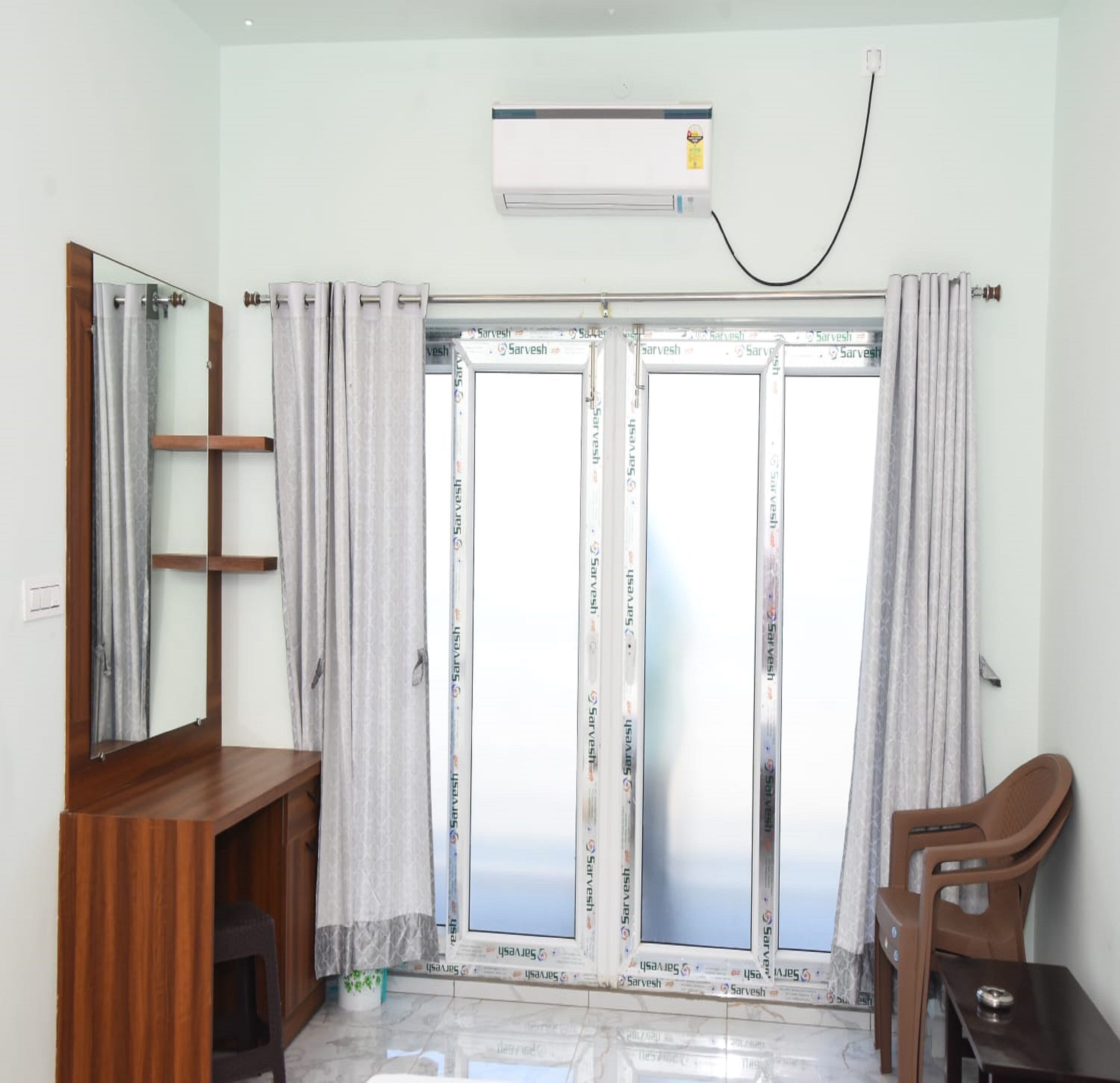 Una stanza con un'ampia porta finestra in vetro, una scrivania in legno, una sedia e un condizionatore d'aria a soffitto.