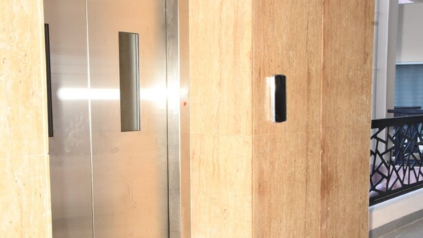 A modern elevator with a metallic finish, adjacent to a wall with a textured surface and a small rectangular object on it. - Maurya Residency (Gingee)