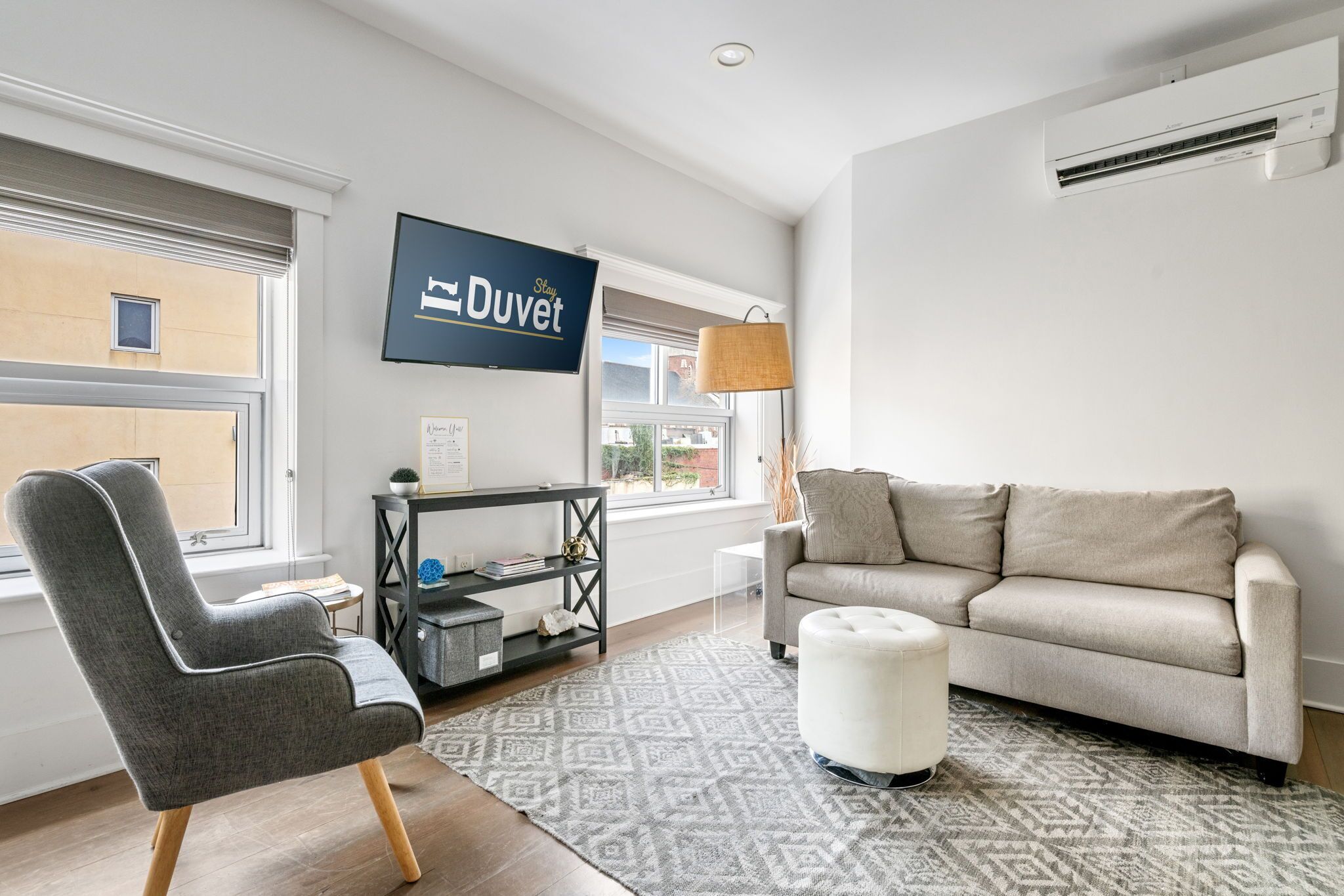 Een moderne woonkamer met een grijze fauteuil, een beige bank en een kamerbreed tapijt met een patroon.