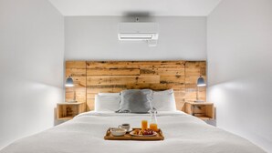 A neatly made bed with a wooden headboard, two bedside tables with lamps, and a tray with breakfast items. - The King Suites at 493 - 8 Suites, 16 Bedrooms (Charleston)
