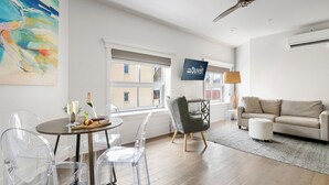 A modern living room with a sofa, a dining table with chairs, a TV, and a large abstract painting. - The King Suites at 493 - 8 Suites, 16 Bedrooms (Charleston)