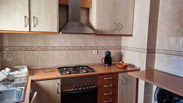 A kitchen with a gas stove, a coffee maker, and a wooden countertop.