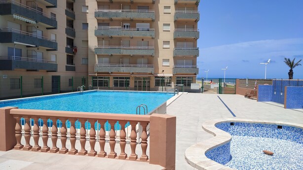 A swimming pool with a tiled deck, a smaller pool with mosaic tiles, and a multi-story building with balconies. - Apartamento muy Fresco Verano (VC)