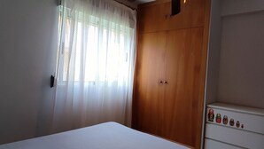 A bedroom with a wooden wardrobe, a bed, and a shelf with decorative items. - Apartamento muy Fresco Verano (VC)