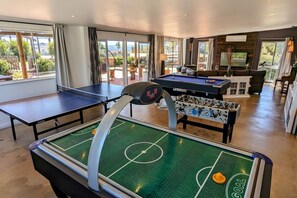 A room with a foosball table, a ping pong table, and a foosball table with a goal.