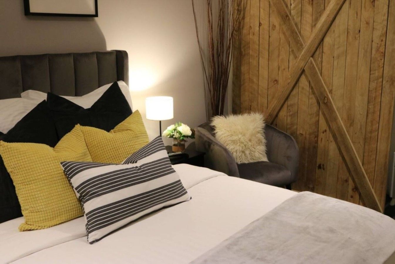 A bed with multiple pillows, a bedside lamp, and a chair with a fur throw.
