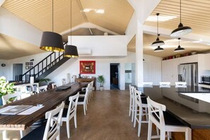 A spacious kitchen with modern appliances, a dining area with white chairs, and a staircase leading to an upper level.