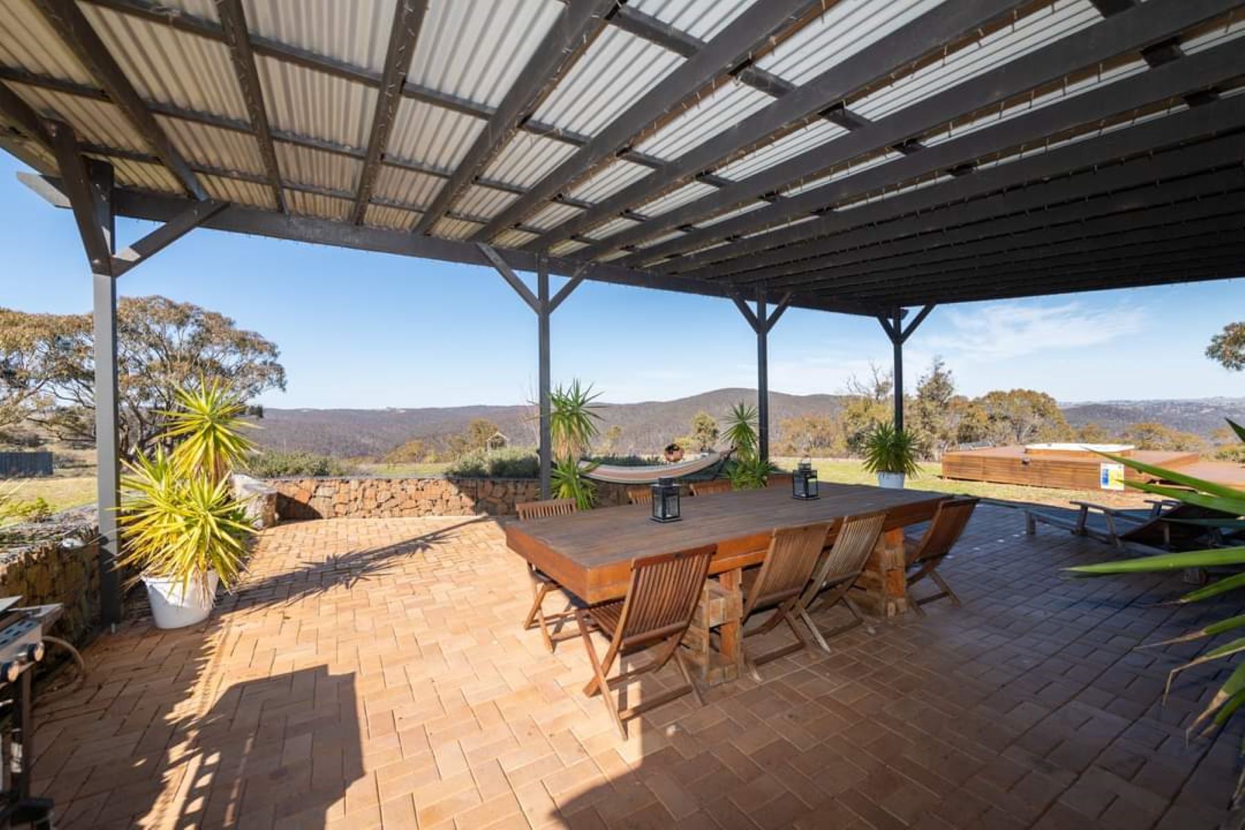 Un patio al aire libre con una mesa y sillas de madera, una hamaca y plantas en macetas.