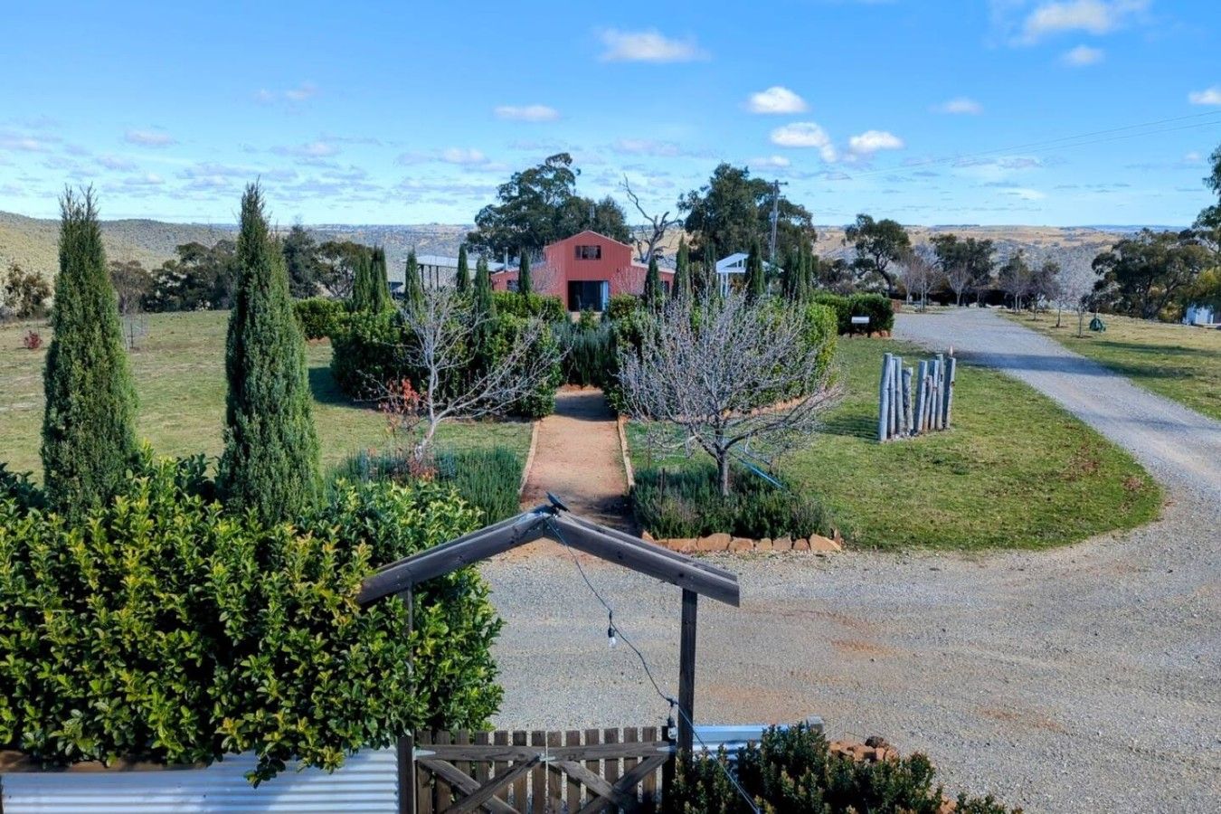Une propriété rurale avec une allée de gravier menant à un bâtiment rouge, entouré de verdure et d’arbres.