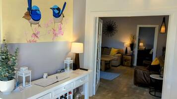 A living room with a white console table, a painting of birds, a potted plant, and a sofa with yellow cushions.