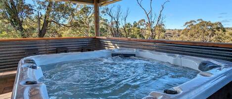 A hot tub under a wooden pergola with a view of trees and hills.