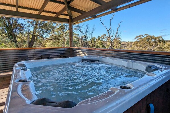 A hot tub under a wooden pergola with a view of trees and hills.