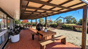 Un patio al aire libre con mesa y sillas de madera, una silla colgante y macetas con plantas.