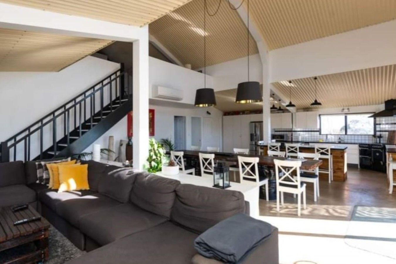 A spacious living area with a large sofa, a staircase, and a kitchen area with bar stools.