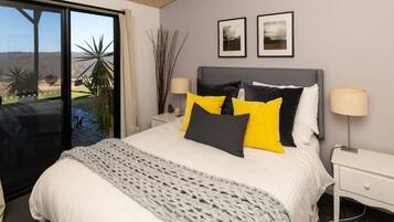 A bedroom with a large bed, two bedside tables, a window with a view, and two framed pictures on the wall.