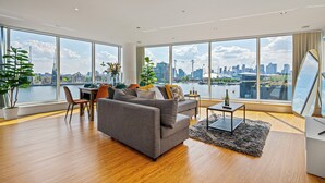 A modern living room with a large window overlooking a cityscape and water. - MARINA VIEW HAVEN- Stylish 2-Bedroom Retreat Near Excel London. (London)
