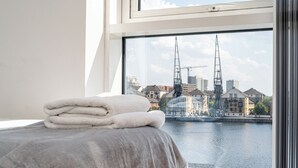A hotel room with a bed, a stack of towels, and a view of a cityscape with buildings and a bridge. - MARINA VIEW HAVEN- Stylish 2-Bedroom Retreat Near Excel London. (London)