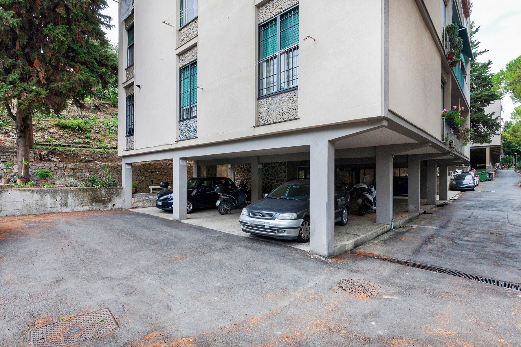 Um edifício com área de estacionamento coberta, paredes de pedra e vasos de plantas.
