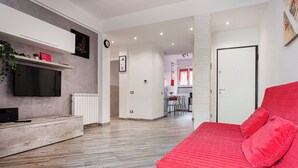 A modern living room with a red sofa, a flat-screen TV mounted on the wall, and a dining area in the background. - La casa di Lorenzo by Wonderful Italy (Genoa)