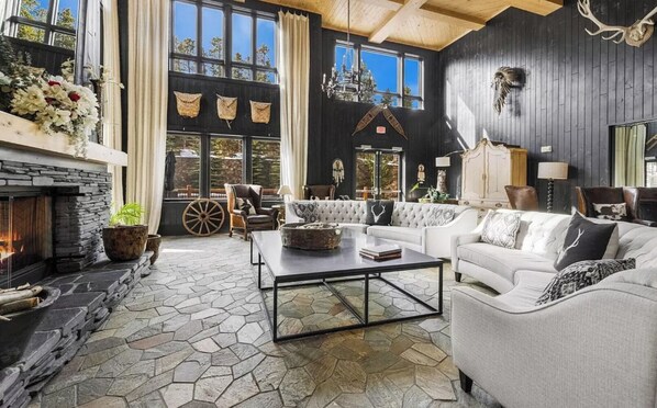 A cozy living room with a stone fireplace, large windows, and a mix of modern and rustic decor. - ✨ Seasons at BlueSky - Lux Penthouse 🏔️ Ski In/Ski Out 🎿 Spa 🧖‍♀️Resort Pool (Breckenridge)