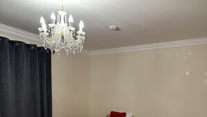Habitación con dos camas de madera, cada una con ropa blanca y detalles rojos, un candelabro y una cortina oscura.