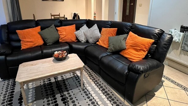 Un sofá de cuero negro con cojines naranja y gris, una mesa de centro de madera y una alfombra con estampado blanco y negro.