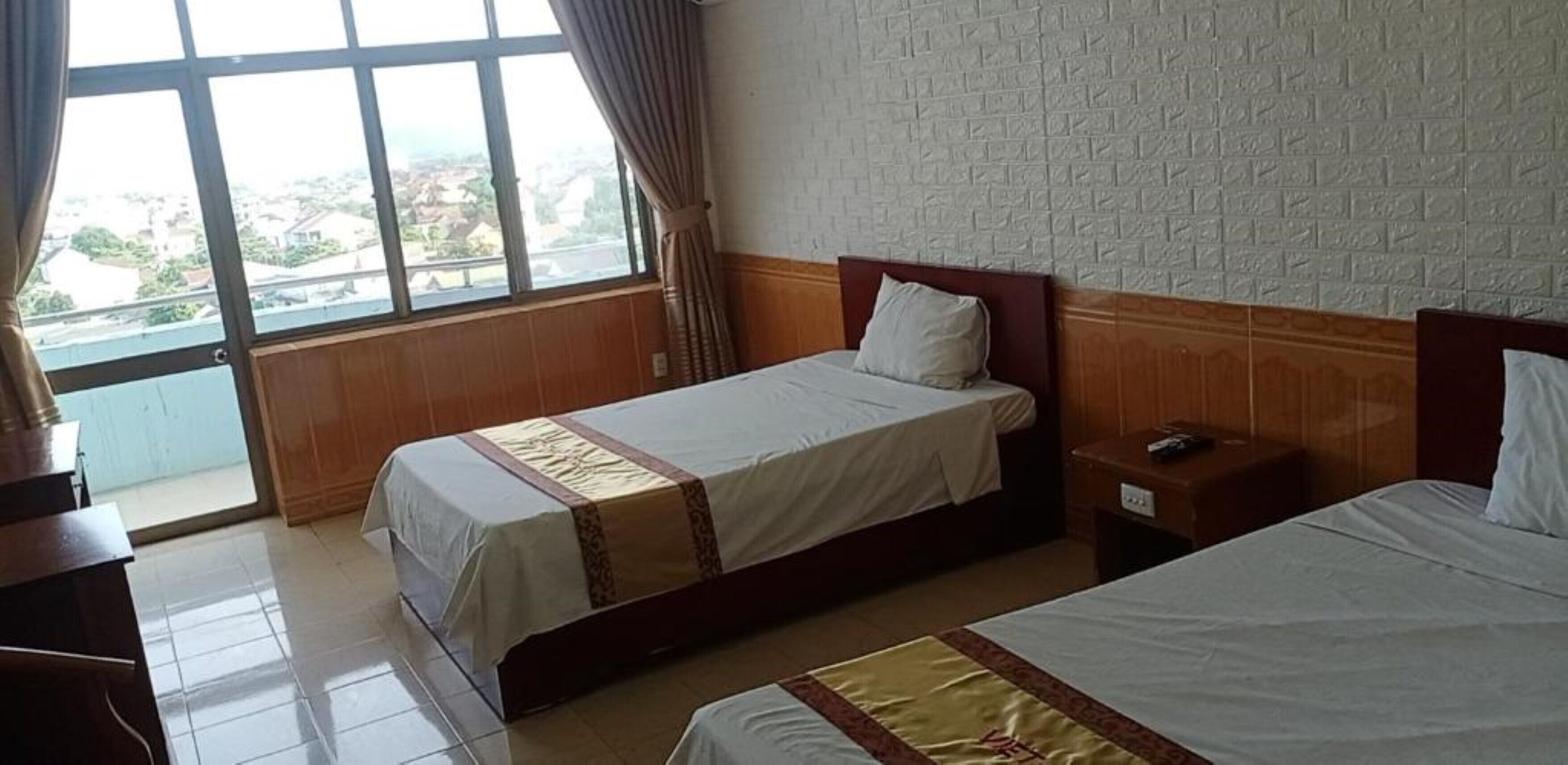 A hotel room with two beds, a wooden headboard, a nightstand, and a window with curtains.