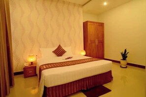Une chambre d’hôtel avec un lit, des tables de chevet, une armoire et une plante en pot.