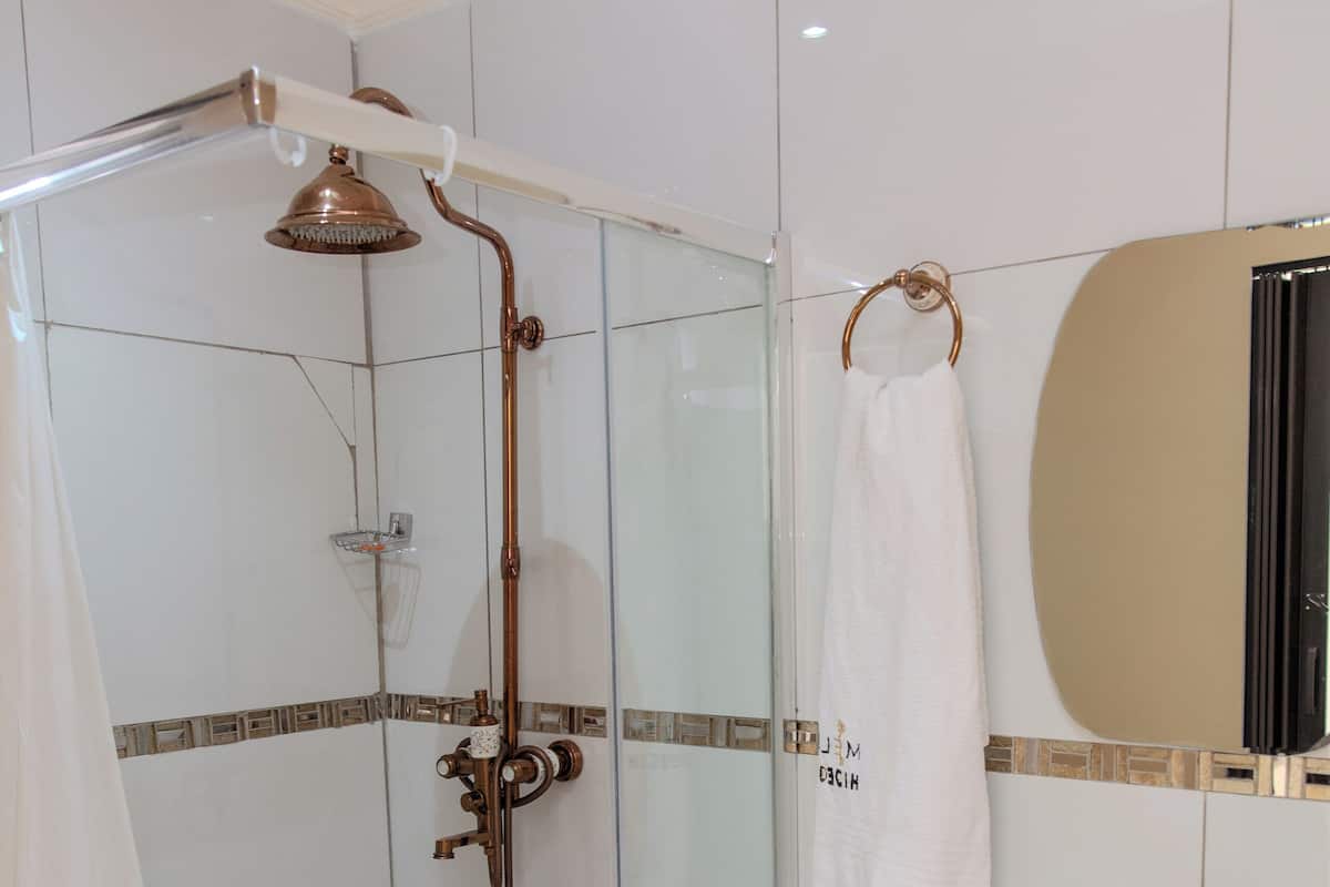 Une salle de bain moderne avec une douche à parois de verre, un lavabo blanc doté d’un robinet en cuivre, et une serviette accrochée au mur.