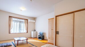 Een kamer met tatami matten, een futonbed, een kleine tafel met een afstandsbediening, een televisie en een kledingkast.