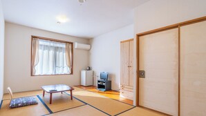 Een traditionele Japanse kamer met tatami vloerbedekking, een futon bed, een televisie en een kleine koelkast.