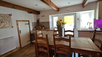 A dining area with a wooden table and chairs, a vase with sunflowers, and a kitchen in the background.