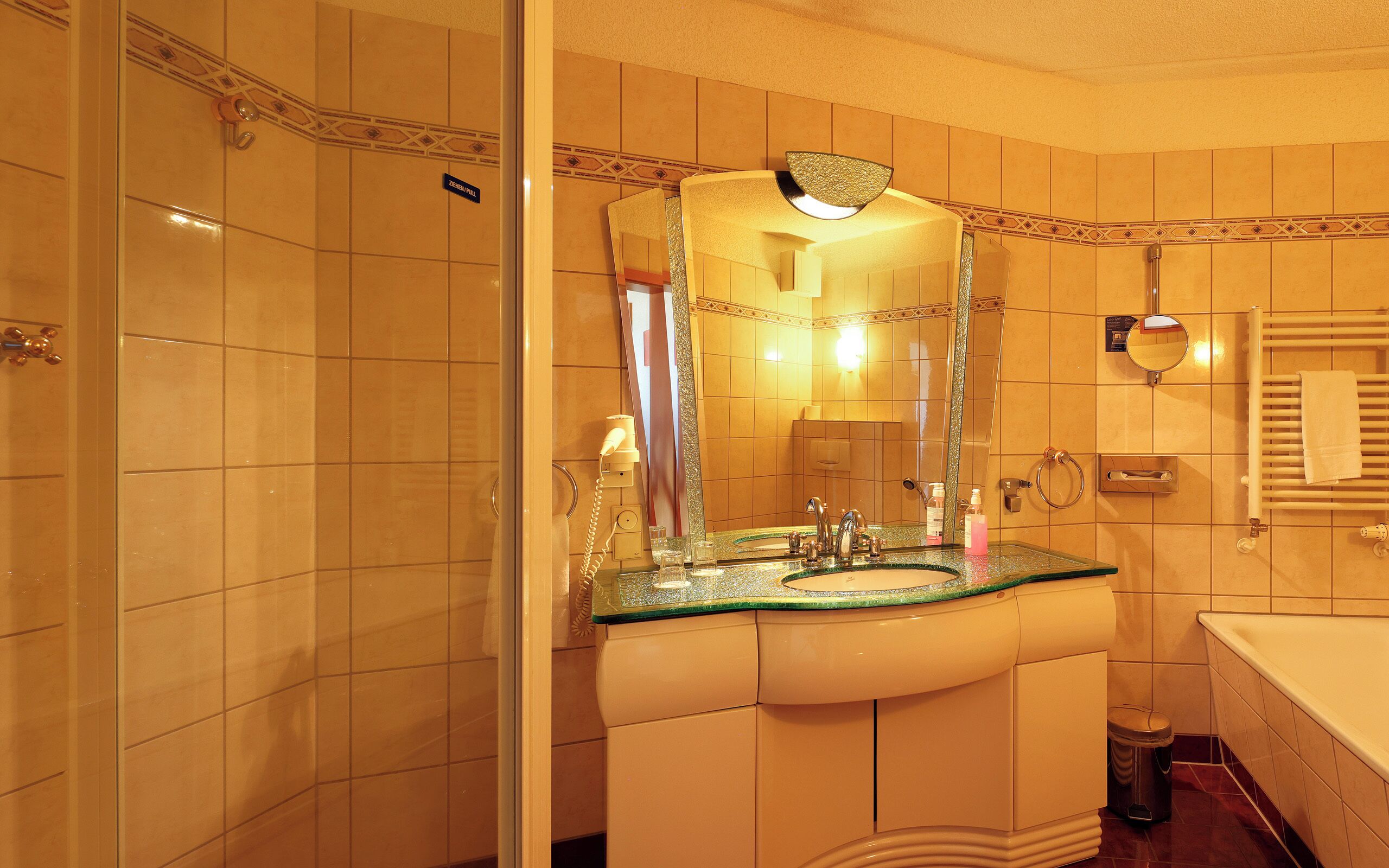A bathroom with a glass-topped sink, a mirror with a decorative frame, a towel rack, and a shower area.