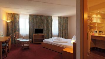 Habitación de hotel con cama, escritorio con silla, televisión y baño visible a través de una puerta abierta.