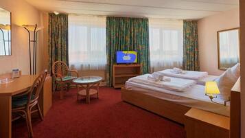 A hotel room with a bed, a desk, a chair, a small table, a television, and curtains.
