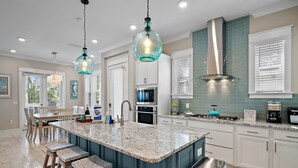 Cocina moderna con una isla central, armarios blancos y salpicadero color turquesa.