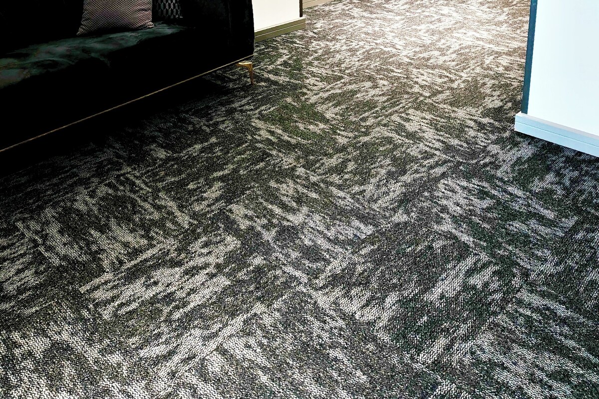 Una habitación con un sofá negro, cojines estampados y suelo alfombrado.