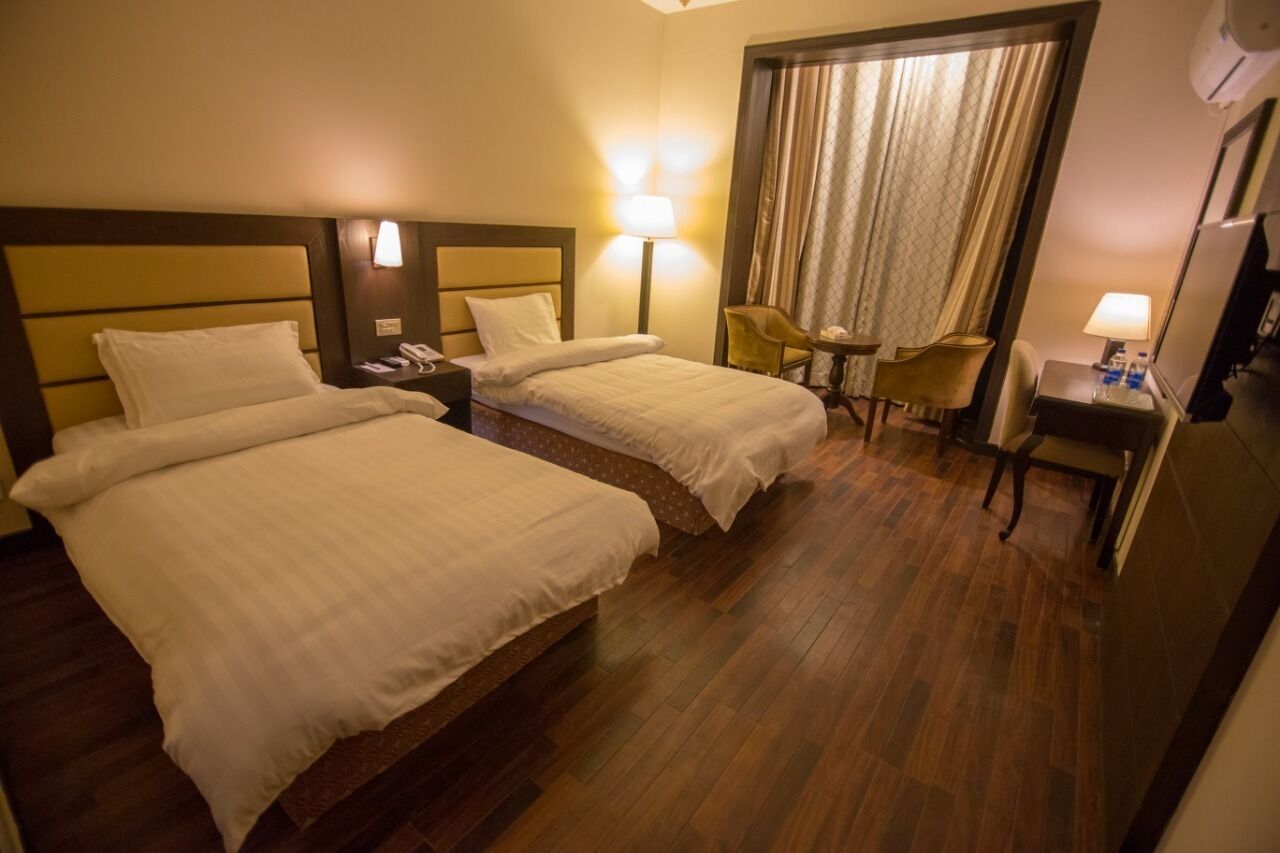 Una habitación de hotel con dos camas, un escritorio, una silla y una mesita de noche con una lámpara.