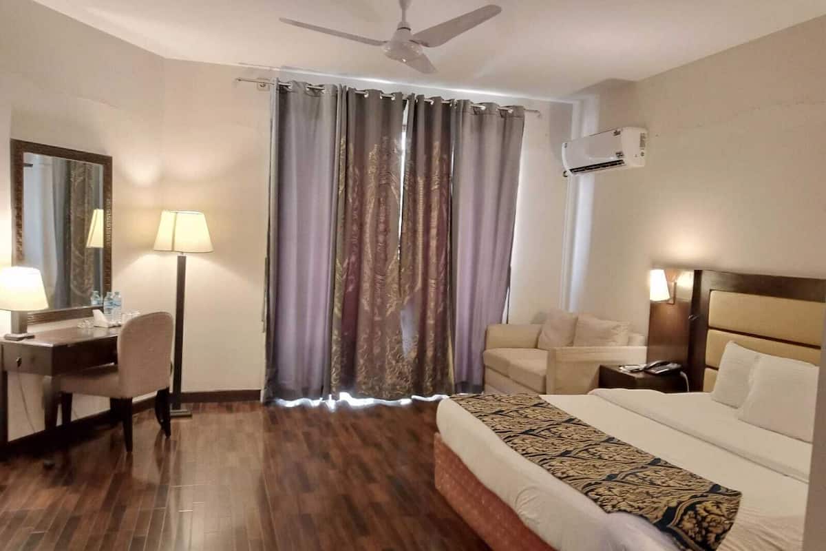 Ein Hotelzimmer mit Bett, Schreibtisch mit Stuhl, Sofa, Deckenventilator und einem Fenster mit Vorhängen.