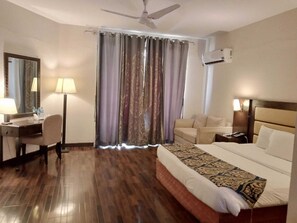 A hotel room with a bed, a desk with a chair, a sofa, a ceiling fan, and a window with curtains. - Hunza Darbar Hotel  (Karimabad)